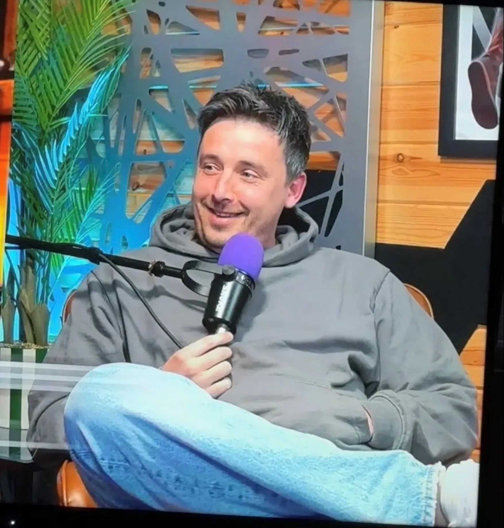 man in jeans and hoodie in front of podcast mic