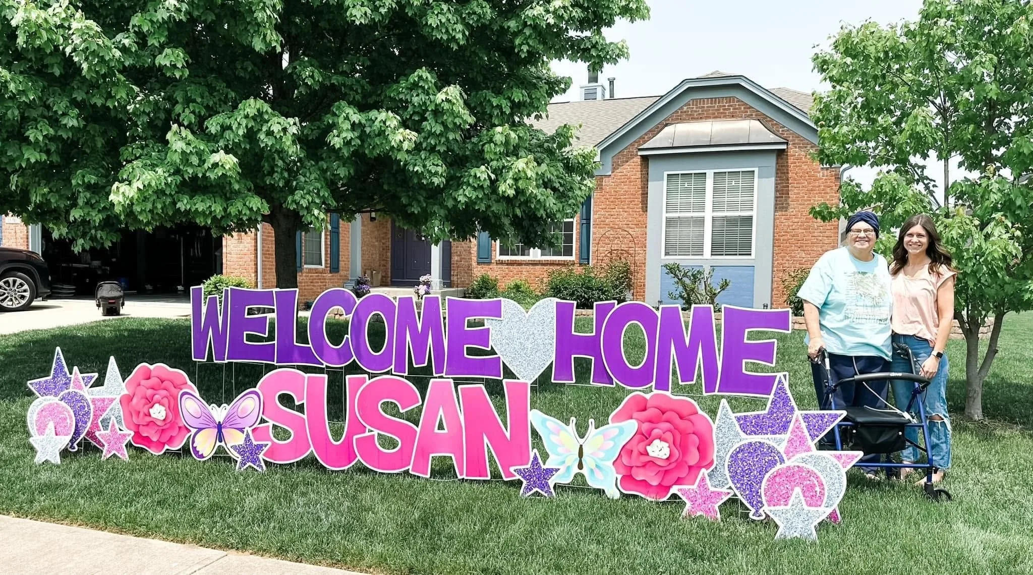 woman with daughter in front yard sign reads 'welcome home susan'
