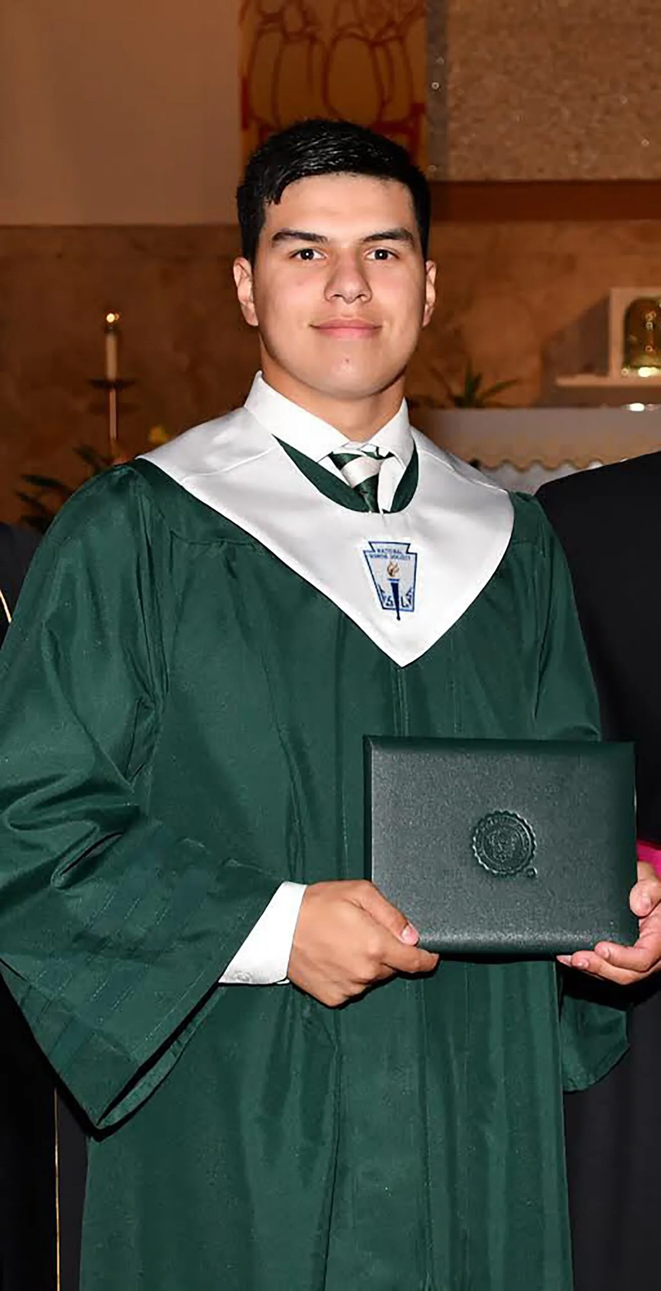 Man wearing green graduation cape, smiling at camera.