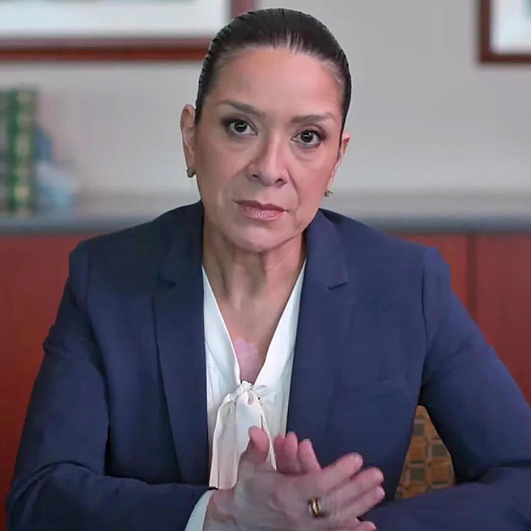 Professional photo of woman wearing blue suit, white top and she's staring at camera.