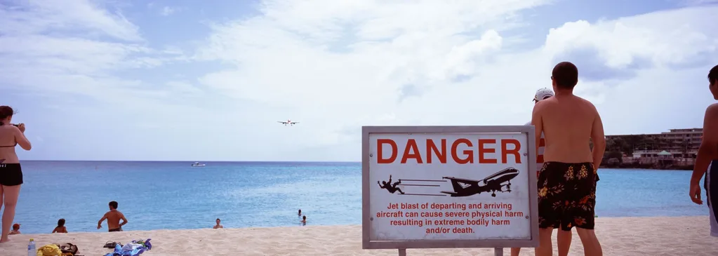 Plane begins descent into Maho Beach with warning sign.