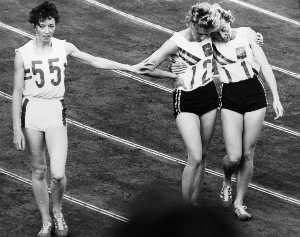 Betty Cuthbert wins gold and walks with the silver and bronze medalists.