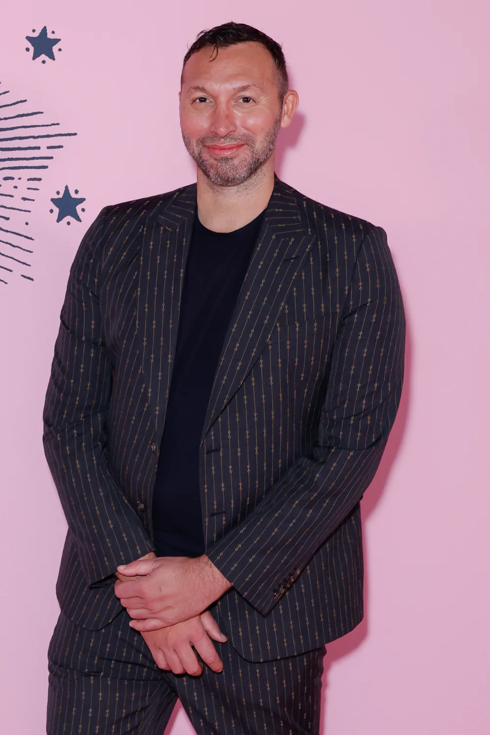 Ian Thorpe wearing a black suit in front of a pink backdrop.