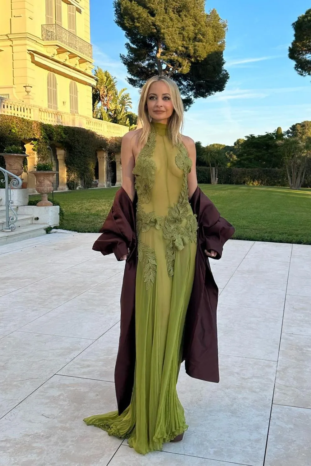 Nicole Richie in a green sheer wedding guest dress outside in a courtyard