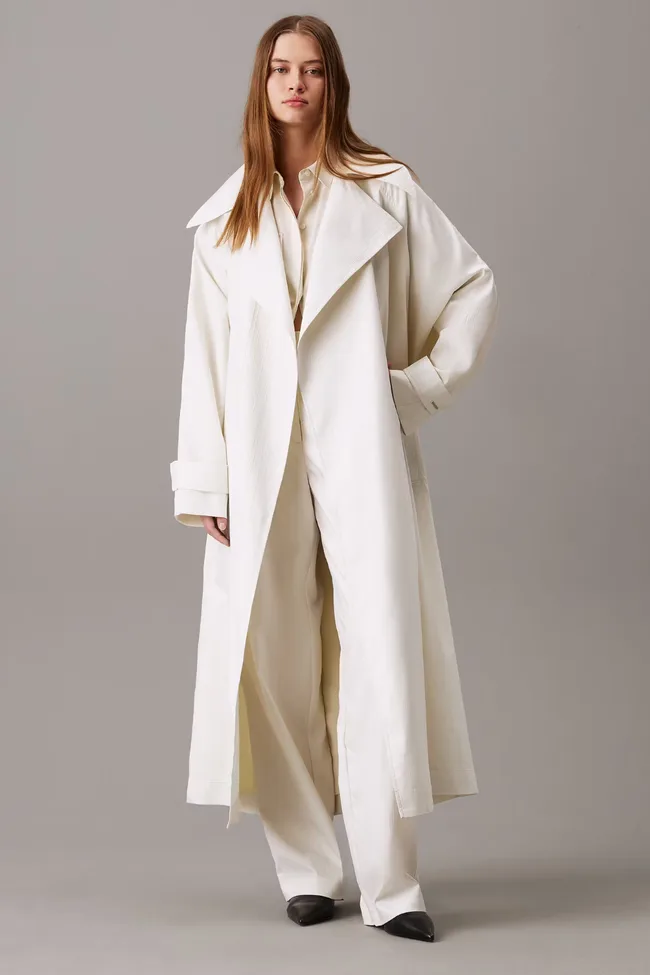 A model wearing a white trench coat by Calvin Klein.