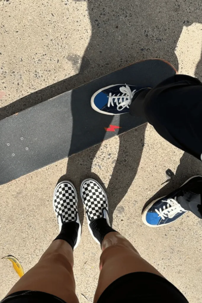 A photo of two people's feet wearing skate sneakers next to a skateboard.