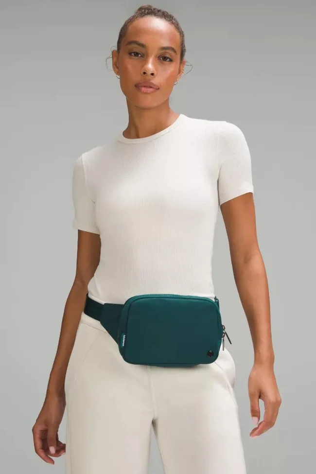 Person in white top and pants wearing a teal waist bag.