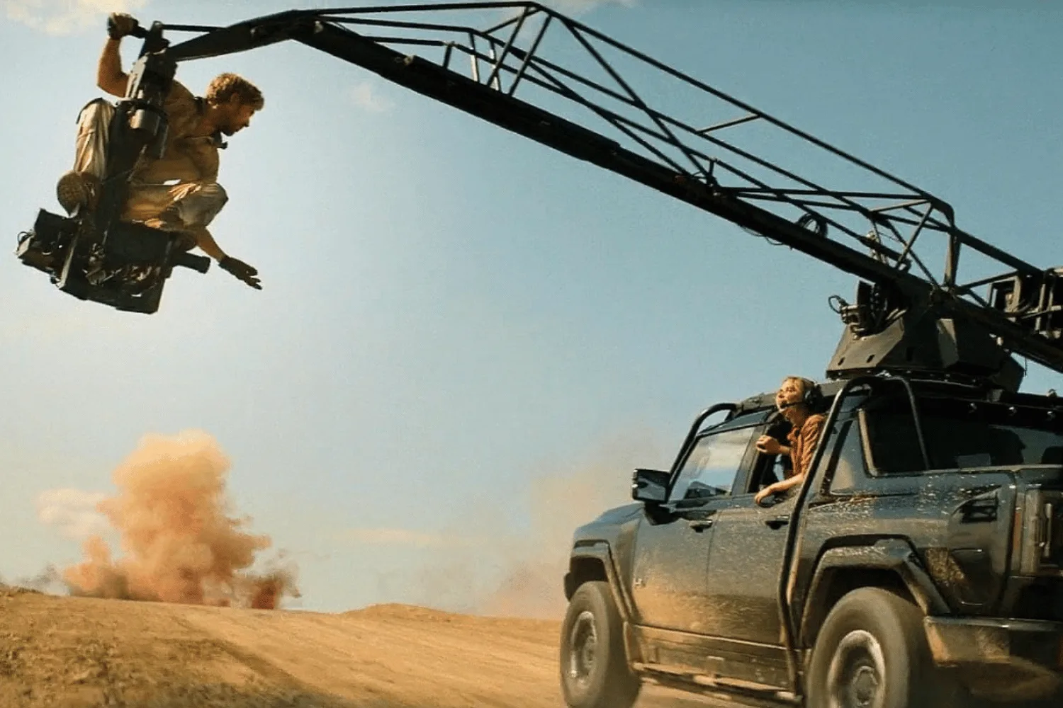 Ryan Gosling sitting on a crane over a car performing a stunt for The Fall Guy. 