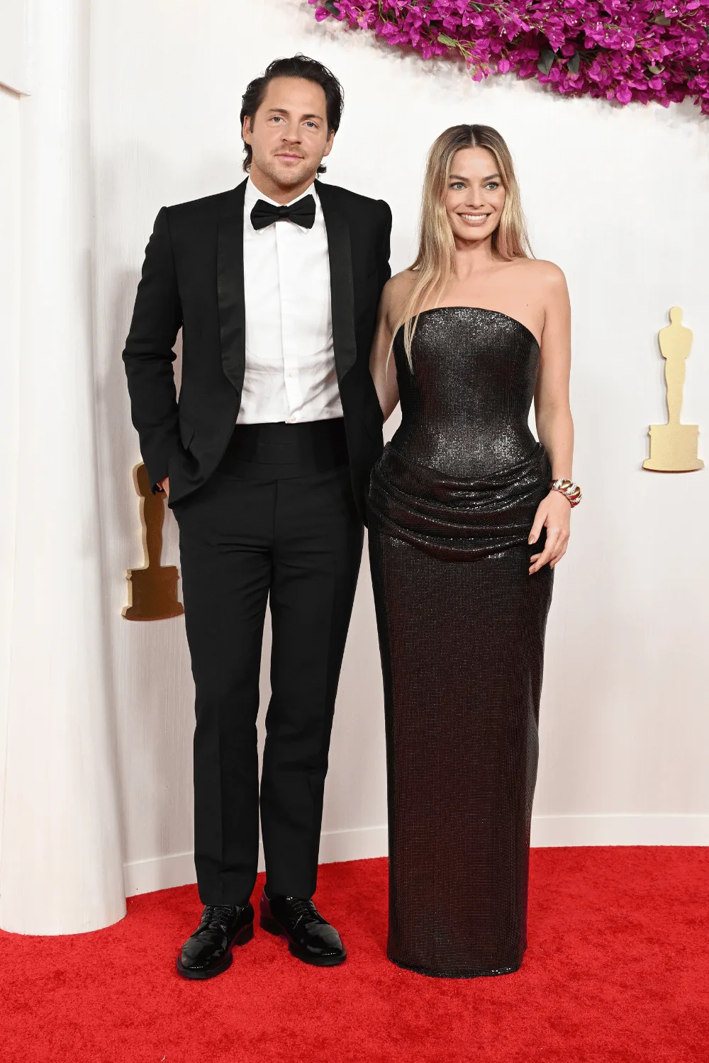 Margot Robbie and Tom Ackerley match in black on red carpet.