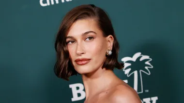Woman with short brown hair and earrings poses against a green background with text and a palm tree logo.