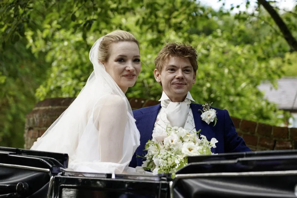 Thomas Brodie-Sangster and Talulah Riley beam in a carriage after their wedding.