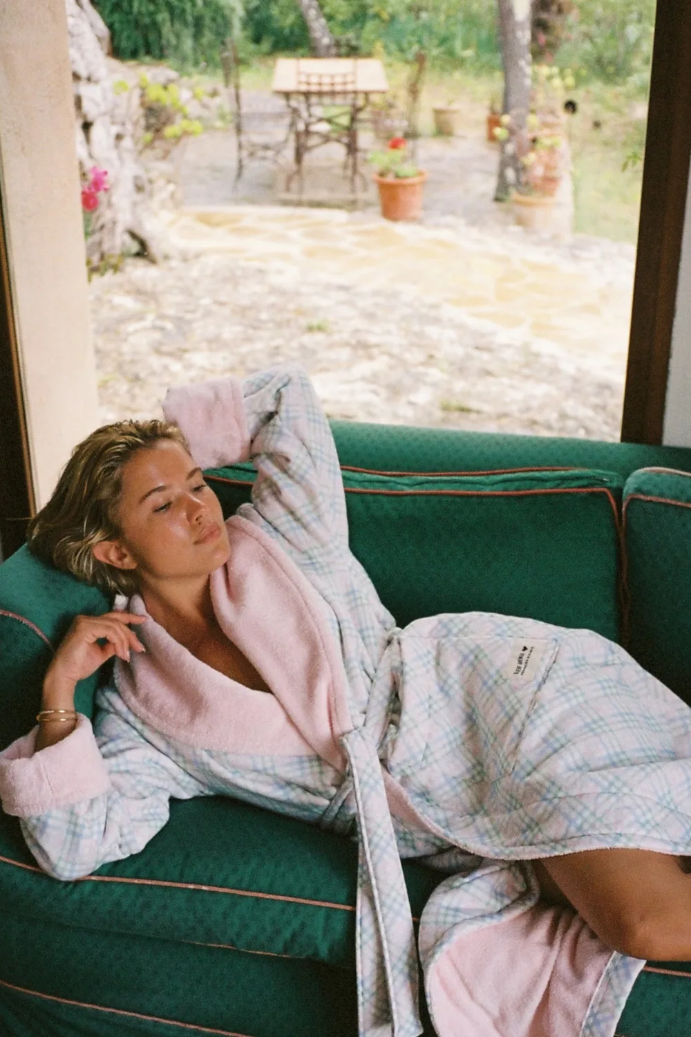 Matilda Djerf on a green lounge wearing a pastel blue and pink robe.