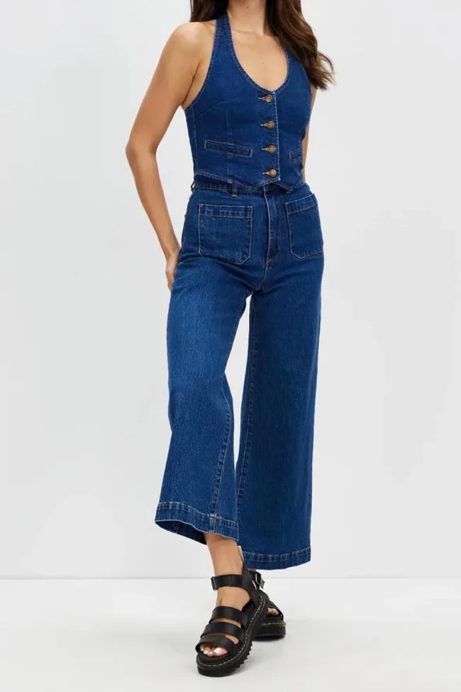 A woman wears a blue denim vest and wide-leg jeans with black sandals.