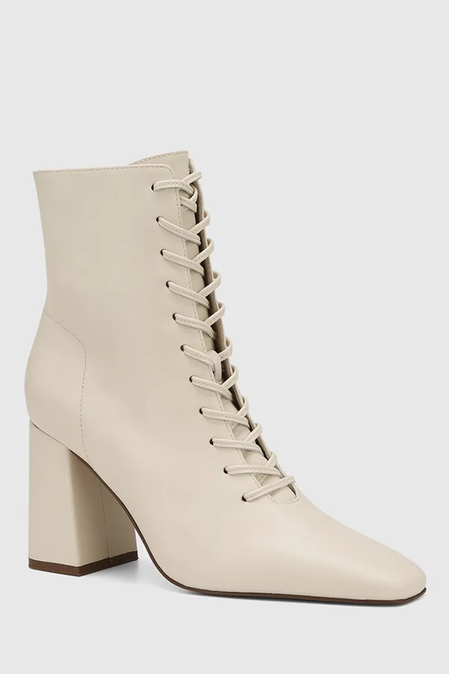 Cream-colored, high-heeled ankle boot with a block heel and lace-up design against a plain background.