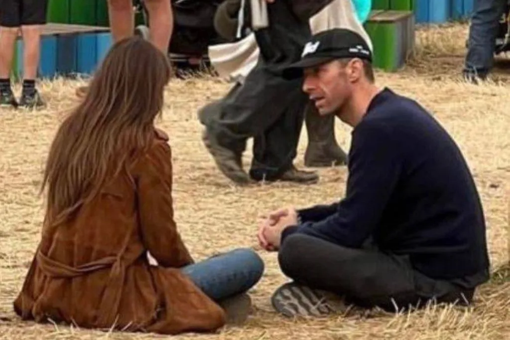Dakota Johnson and Chris Martin sitting on the ground at Glastonbury.