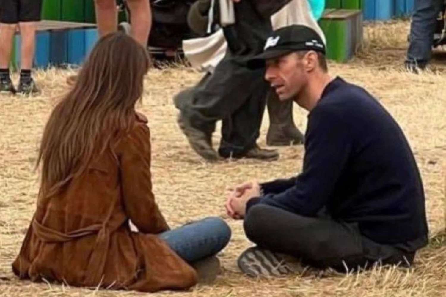 Dakota Johnson and Chris Martin sitting on the ground at Glastonbury.
