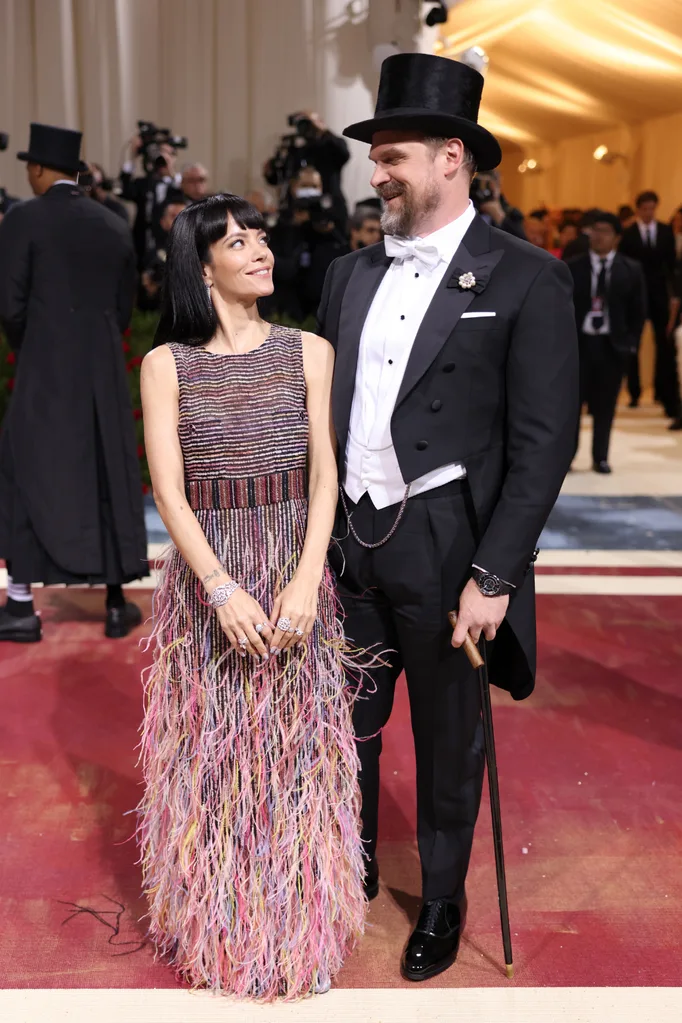 Couple in formal attire at a gala, with her in a colorful fringe dress and him in a tuxedo and top hat with a cane.