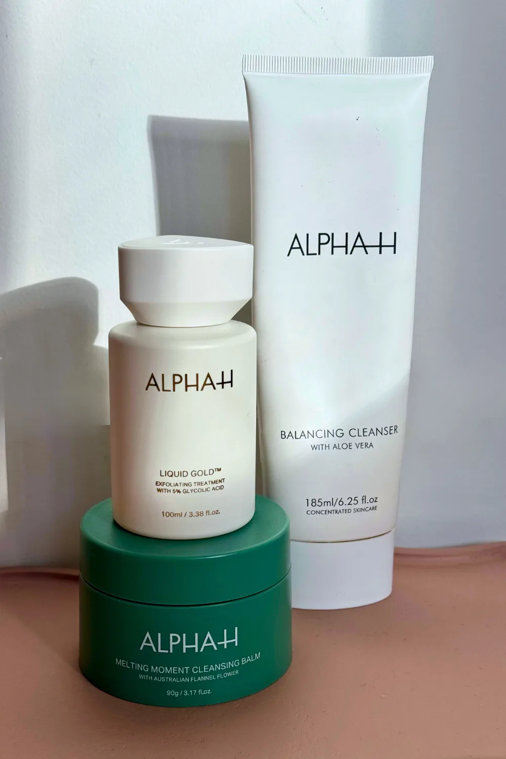 Three ALPHA-H skincare products stacked on pink tray.