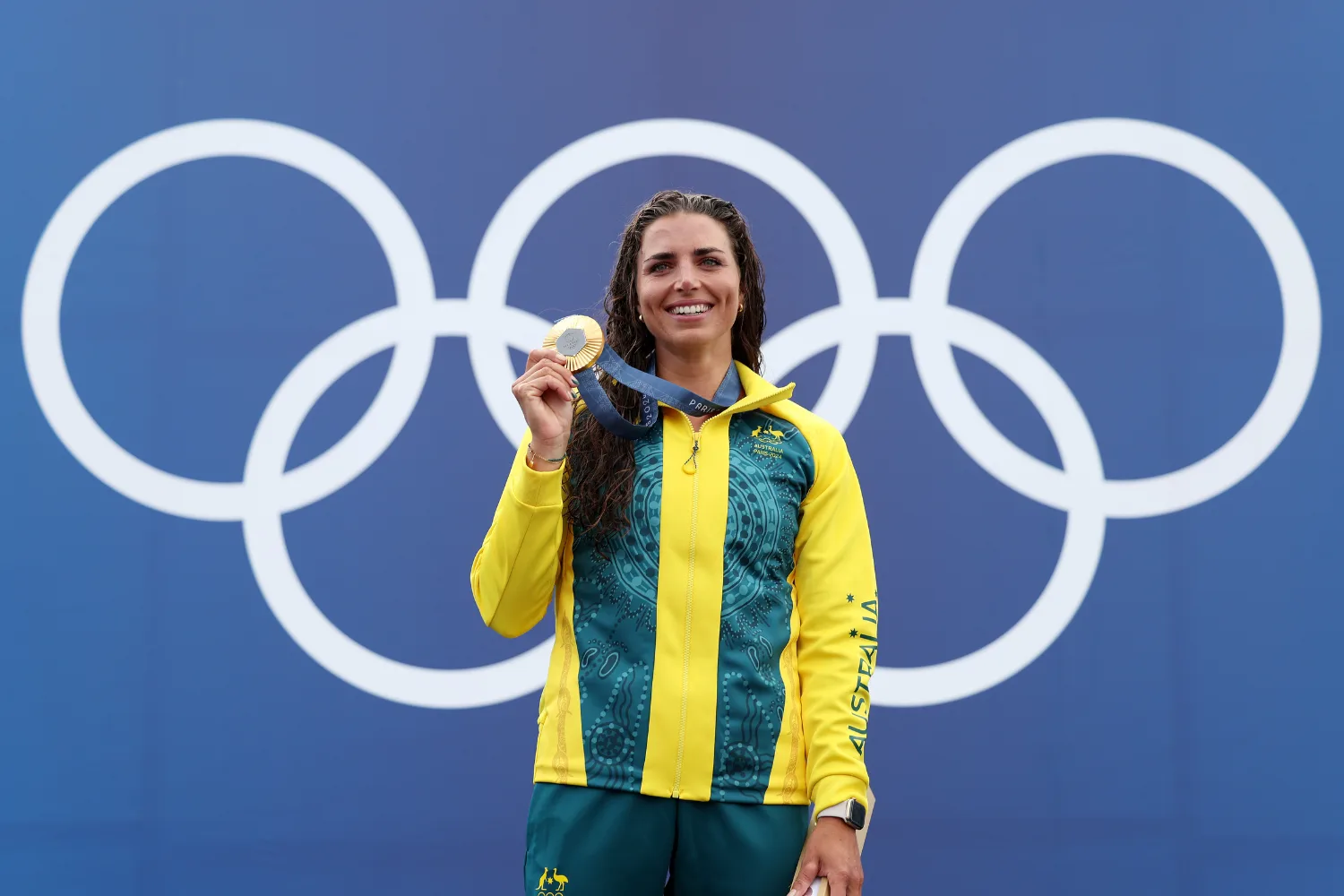Jessica Fox holding a gold medal in front of the olympic rings.