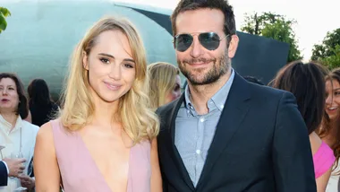 Two people smiling at an outdoor event, one wearing sunglasses and a suit, the other in a pink dress.