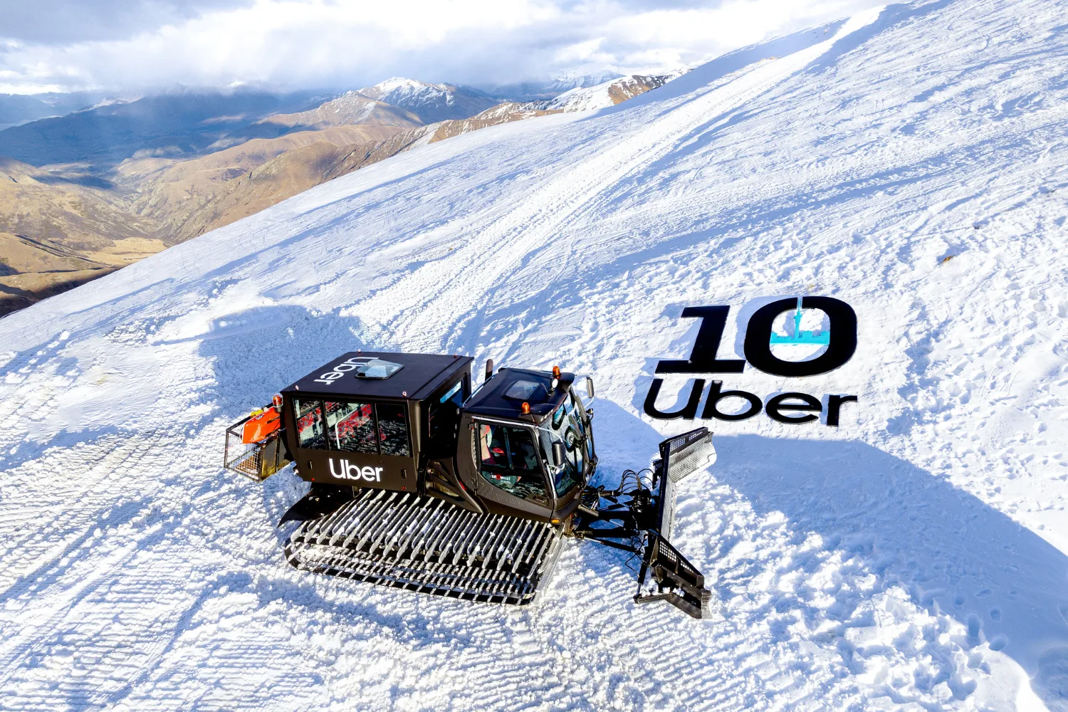 A snow cat on the snow next to a black sign that says 10 Uber. 