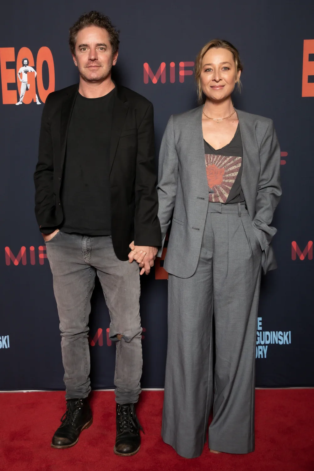 Asher Keddie and Vincent Fantauzzo holding hands on a red carpet.