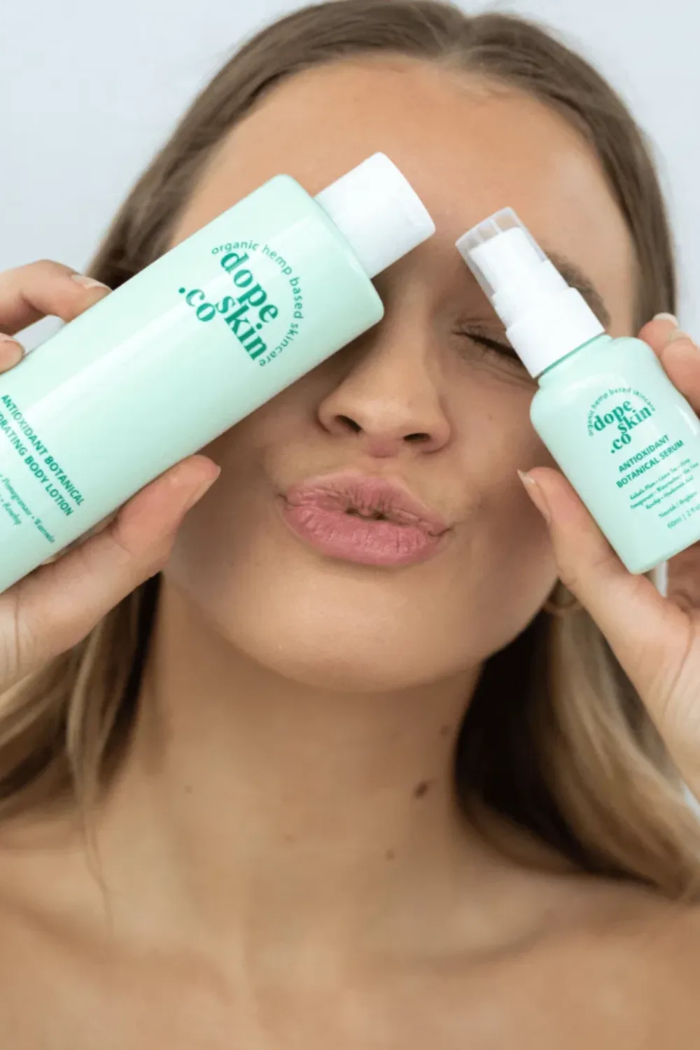 A model holding two mint green bottles of Dope Skin Co against her eyes.
