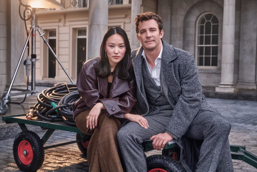 Yerin Ha and Luke Thompson sitting on a green flatbed trolley on the set of Bridgerton season four.