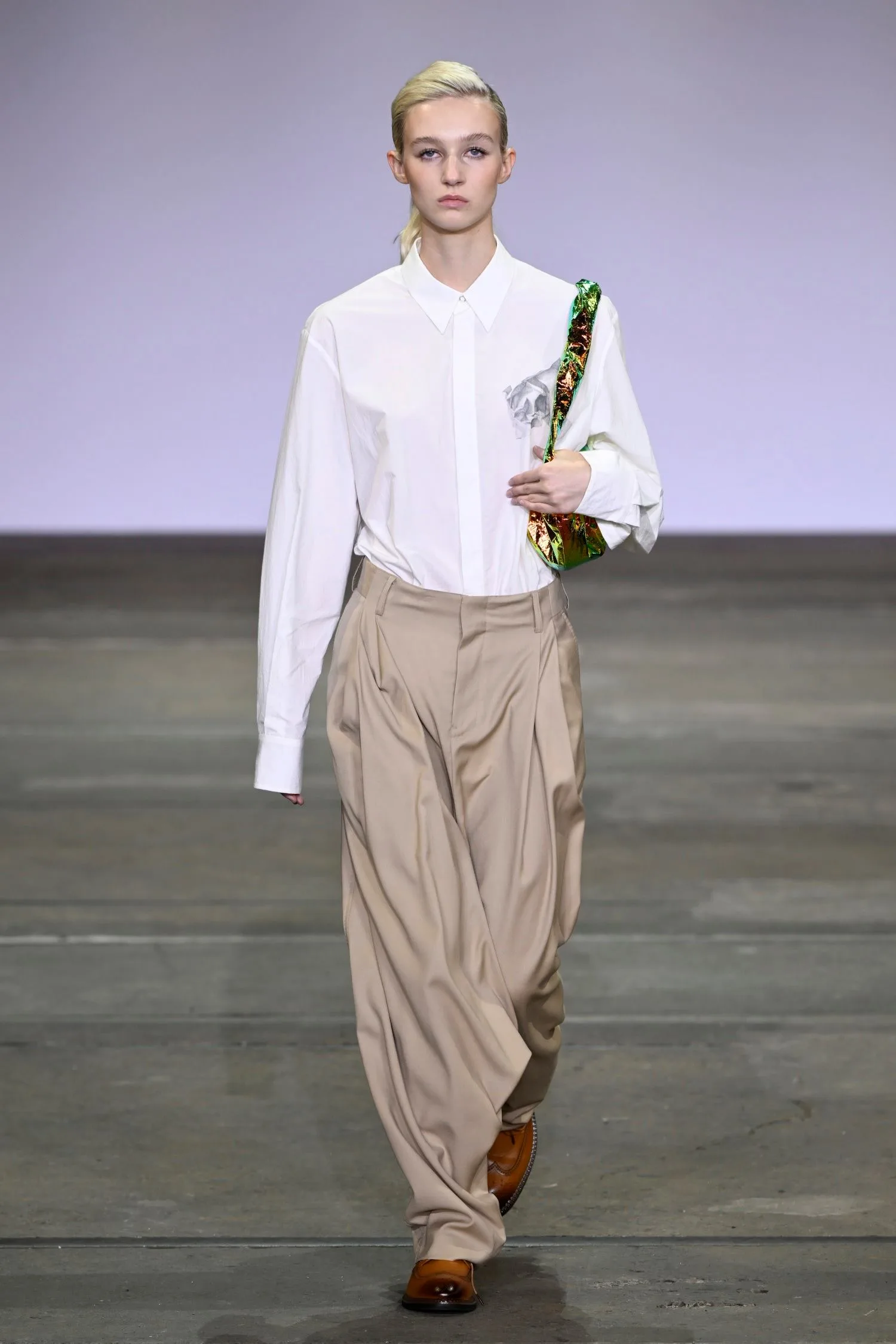 Allegra Overton wears a white shirt and tan pants on the catwalk