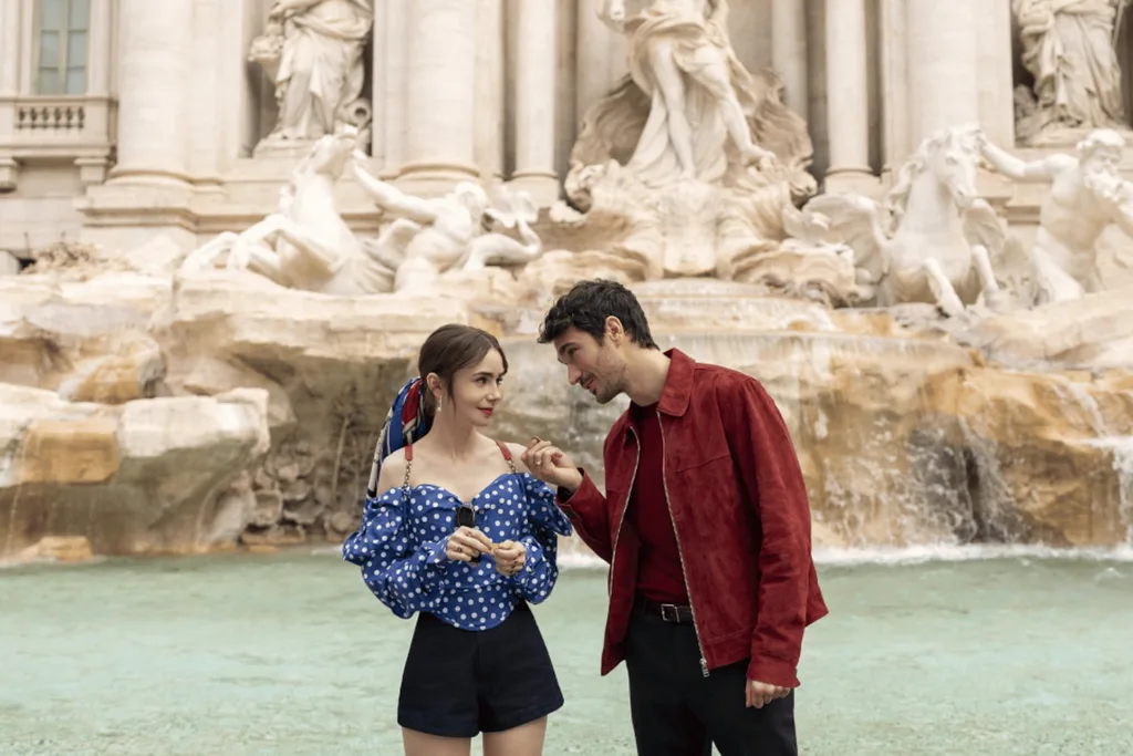 Emily in Paris characters Emily and Marcello standing in front of the Trevi Fountain.