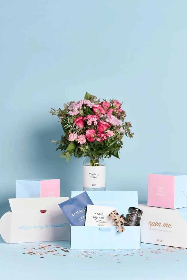 A bouquet of flowers on a blue background surrounded by a bridesmaid hamper.