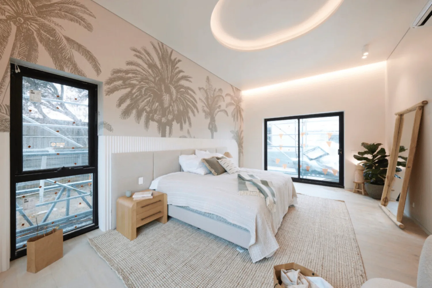 A white bed in the middle of a bedroom with beige palm tree wallpaper