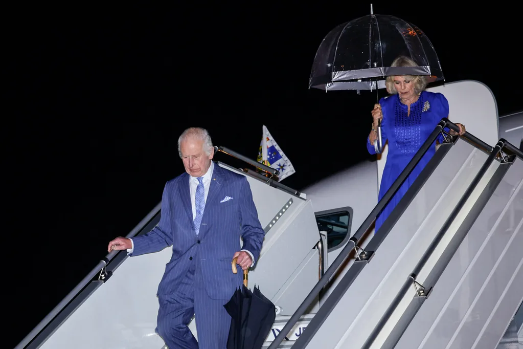 King Charles and Queen Camilla arrive on a rainy night