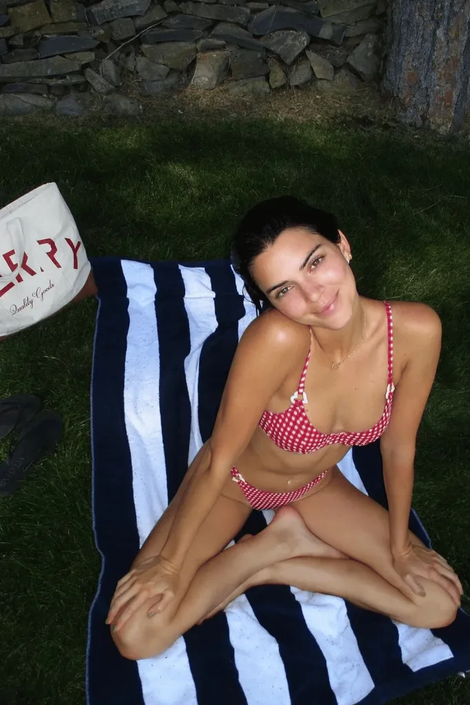 Kendall Jenner sitting cross legged wearing a red gingham bikini