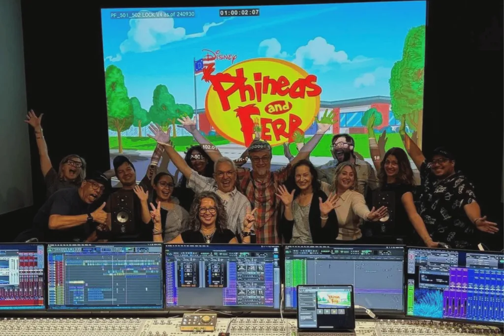 The crew of Phineas and Ferb standing togeher in a recording booth.