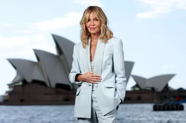 Connie Nielsen wears a blue suit and is standing in front of the Sydney Opera House