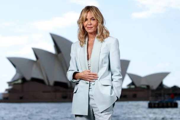 Connie Nielsen wears a blue suit and is standing in front of the Sydney Opera House