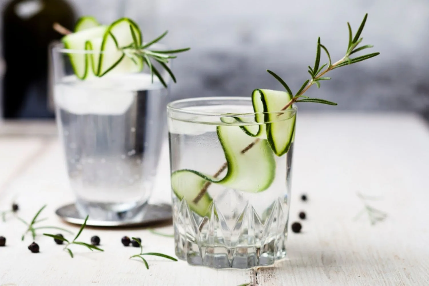 Two glasses of gin and tonics with cucumber and rosemary garnish