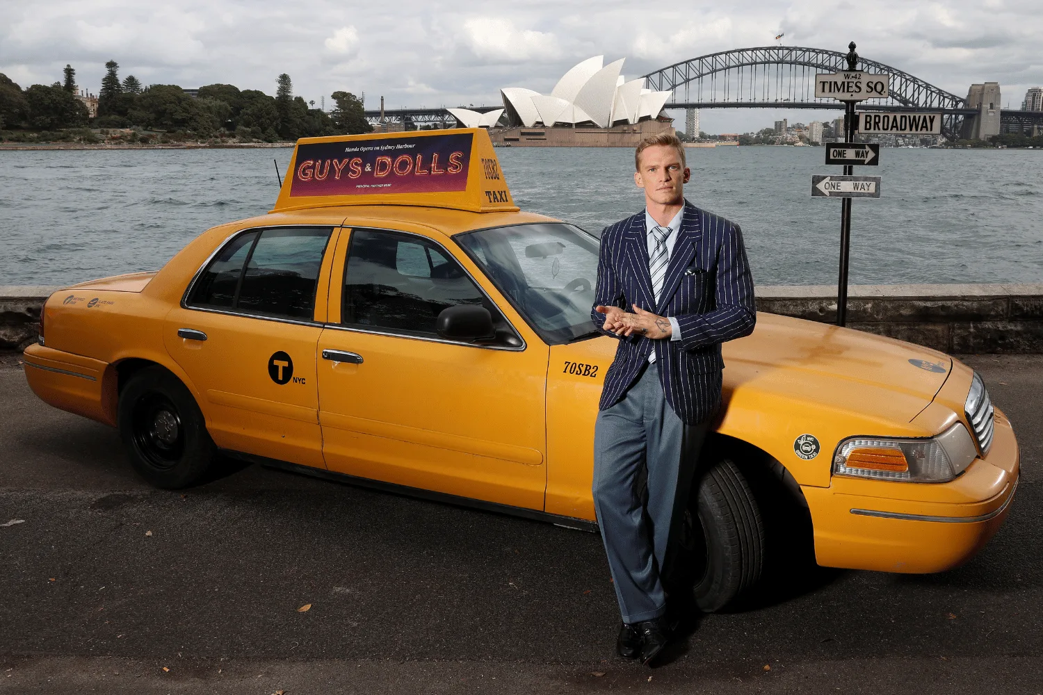 Cody Simpson leaning against a yellow New York taxi across from the Sydney Harbour Bridge.