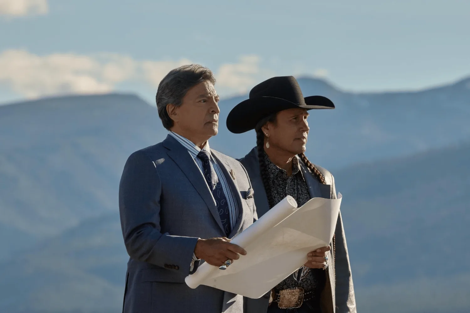 Two people standing in front of a mountain range. 