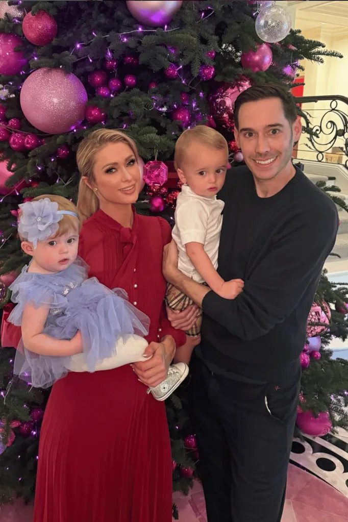 Paris Hilton with her husband and their two kids standing in front of a Christmas tree.
