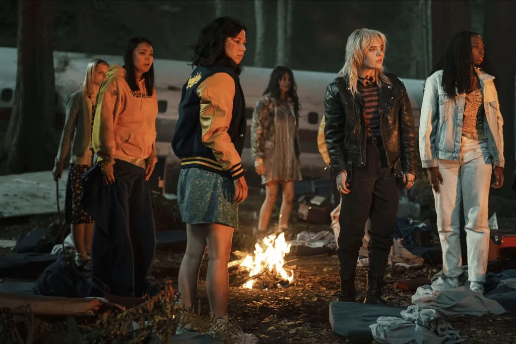 The team from Yellowjackets standing around a campfire.