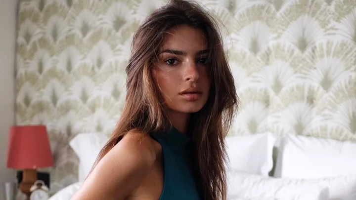 Emily Ratajkowski sitting on the edge of a bed in activewear