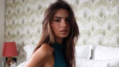 Emily Ratajkowski sitting on the edge of a bed in activewear