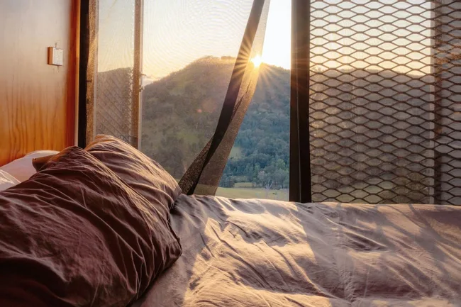 Tiny Home Mansfield bed next to window overlooking a sunrise.