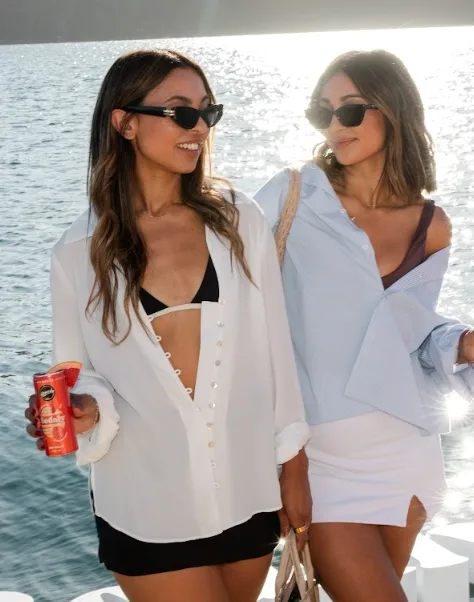 Two young women in white shirts hold cans of sodaly soft drink