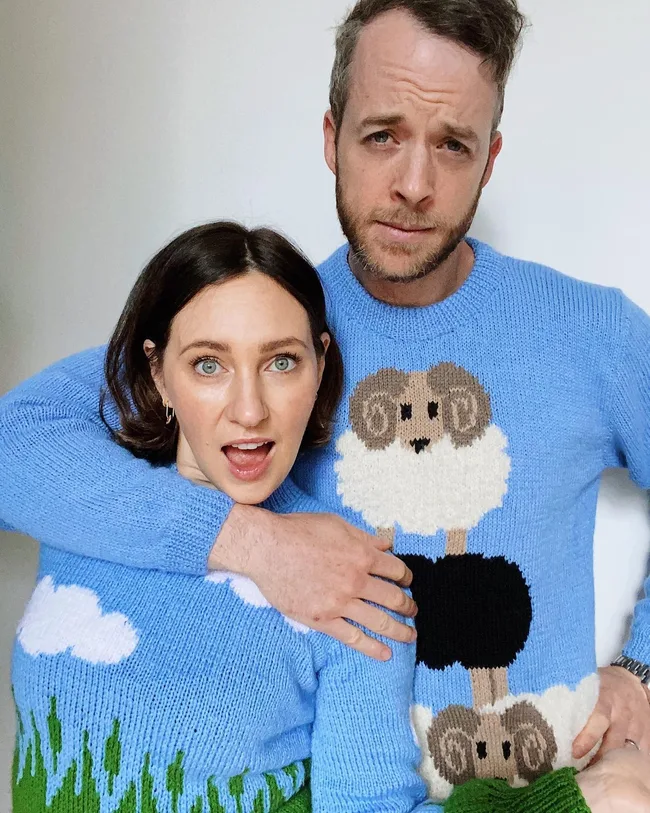 Hamish Blake wraps one arm around Zoe Foster Blake as the two show off their very similarly knitted sweaters with a blue sky and clouds pattern.