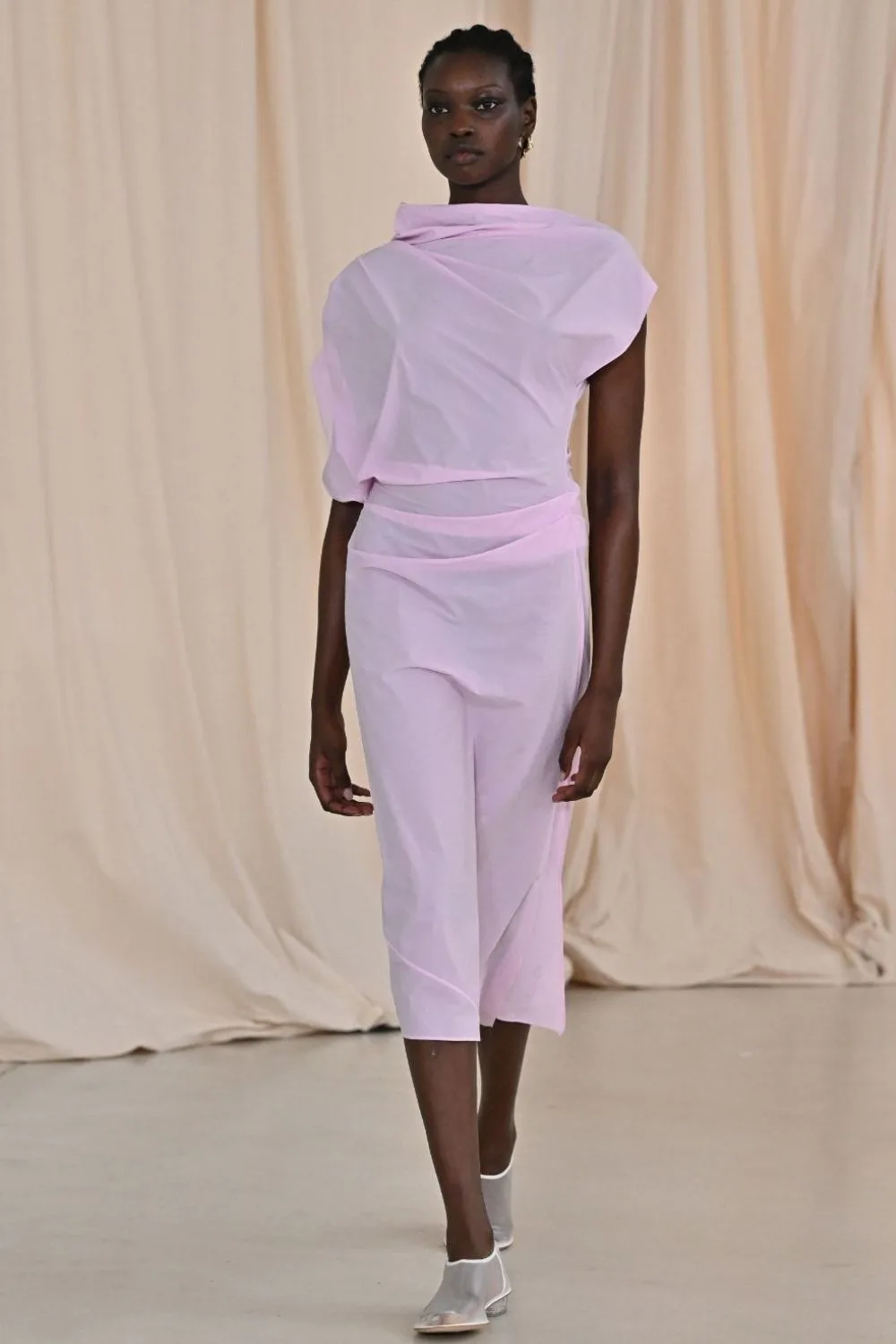 Model walks a runway in a sheer pink dress