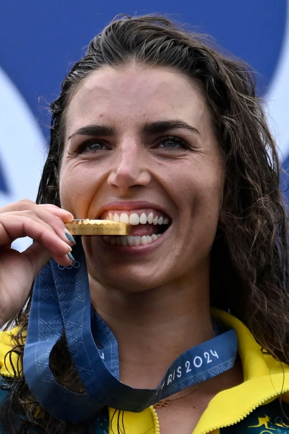Jess Fox at the olympics biting her gold medal and smiling.