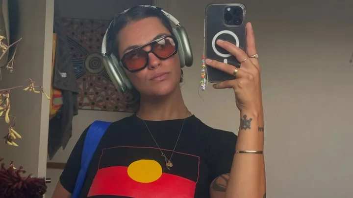 Sianna Catullo taking a selfie in front of a mirror wearing First Nation flag t-shirt.